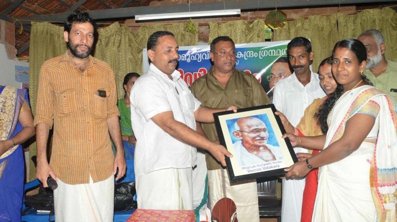 A file photo of K. Sajeevan handing over a portrait of Mahatma Gandhi to Narippatta Samoohya Vihara Kendram library. By arrangement