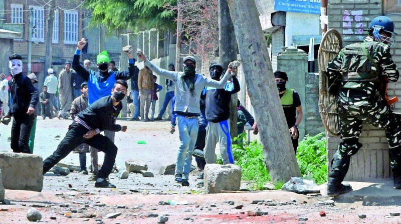 Protesters throw stones on security men outside a poling station during the bypoll in Srinagar on Sunday.