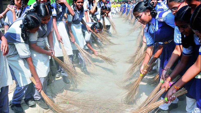 Some students cover their faces to protect themselves from the dust raised by about 2,500 students sweeping the ground at Parsigutta. They were part of a  Swachh Bharat promotion effort and made a bid for a Guinness record. (Photo: DC)
