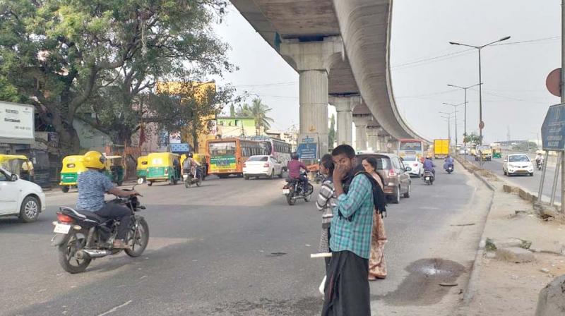 Due to lack of bus shelters, pedestrians have to wait for buses on the road