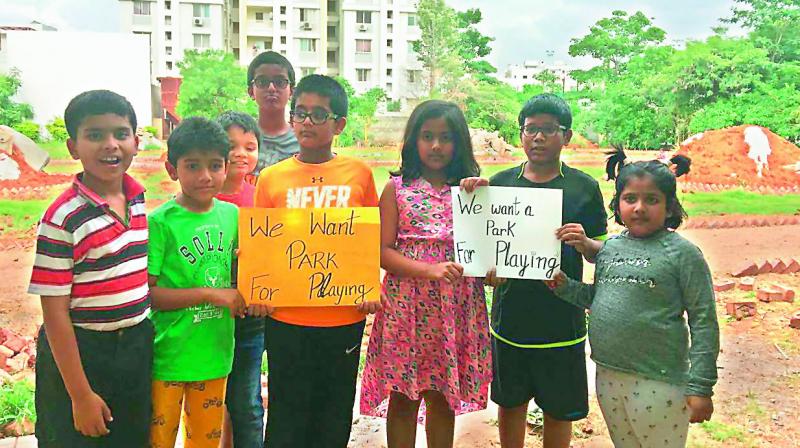 Children aged eight and 12 hold posters asking for the park to be returned so that they can play again. In the backdrop one can see building material dumped in the park.