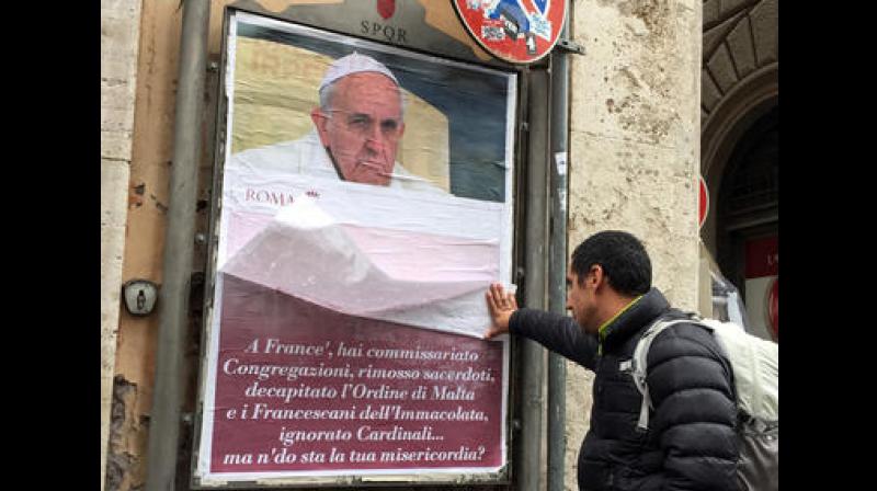 A passerby lifts a paper sheet covering an anti-Pope Francis poster to read it, in central Rome. (Photo: AP)