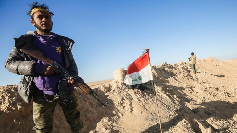A fighter of the Hashed al-Shaabi paramilitaries poses for a picture carrying a Kalashnikov assault rifle next to an Iraqi flag at a defensive position near the frontline village of Ayn al-Hisan, on the outskirts of Tal Afar west of Mosul. (Photo: AFP)