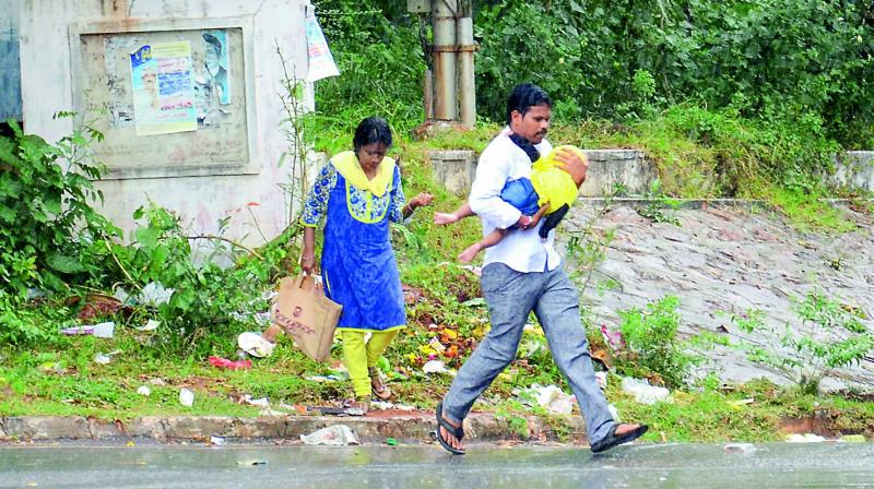 A family runs for the cover during a sudden downpour, in Visakhapatnam on Thursday. (Photo: DC)