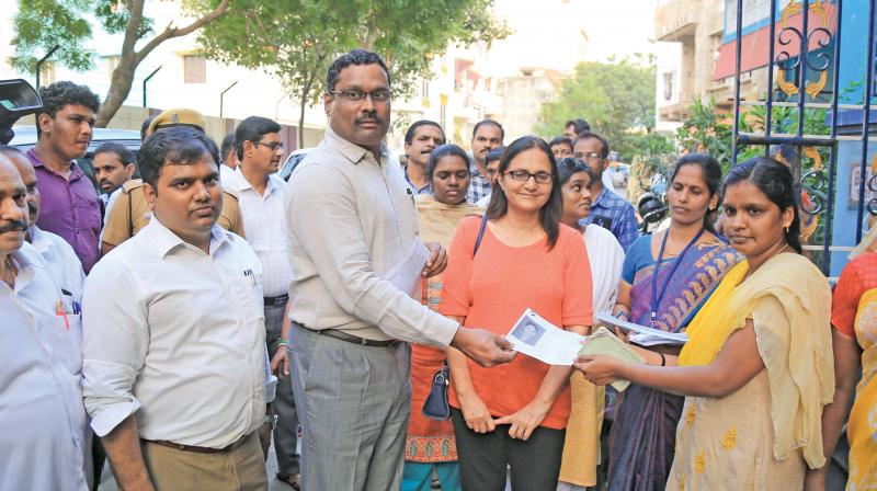District election officer D. Karthikeyan distributes booth slips with photo ahead of RK Nagar bypoll at TNEB quarters in Thiruvalluvar Nagar on Tuesday. (Photo: DC)