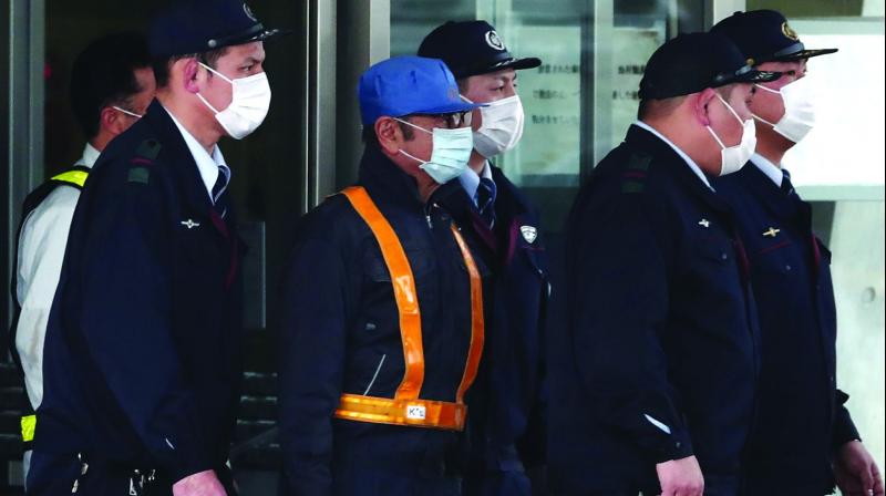 Ousted Nissan chief Carlos Ghosn, wearing a blue cap, is escorted out of the Tokyo Detention House in Tokyo on Wednesday