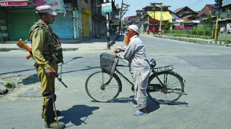 A security personnel stops a cyclist during curfew in Srinagar on Sunday. (Photo: PTI)