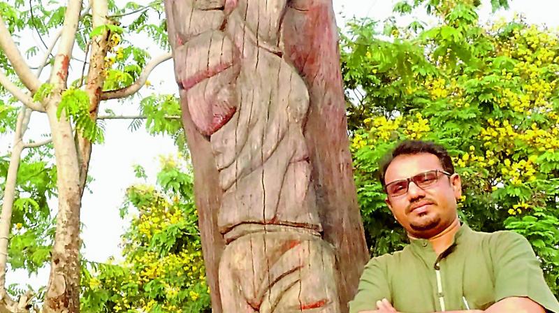 Artist Narasinga Rao with the wood  sculpture of a basketball player etched right into the tree.