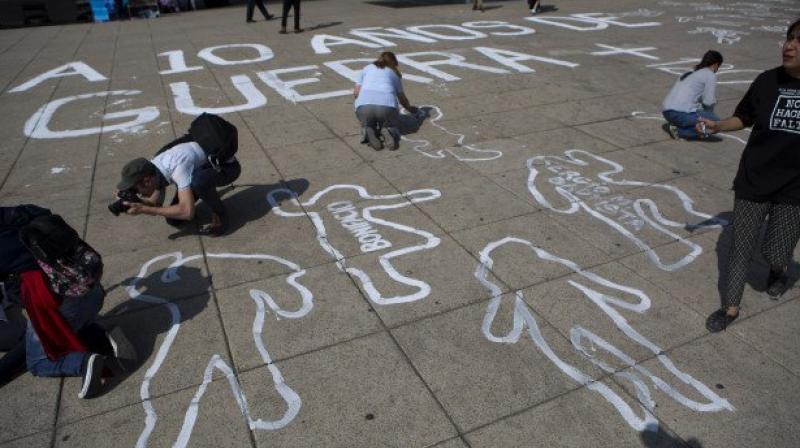 People paint outlines of bodies as part of a memorial for those killed, on the 10th anniversary of the drug wars start, at the Monument for the the Mexican Revolution, in Mexico City. (Photo: AP)