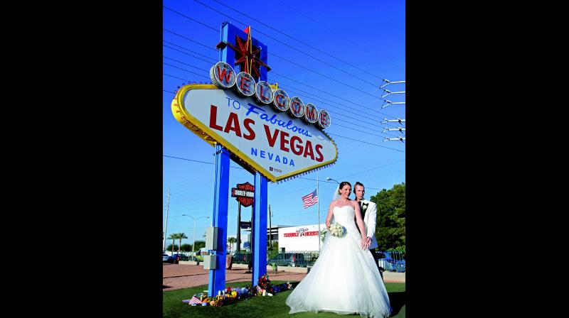 A newlywed couple of Germany poses for photos in front of the Welcome to Las Vegas sign that has flowers honoring the people who died in the mass shooting