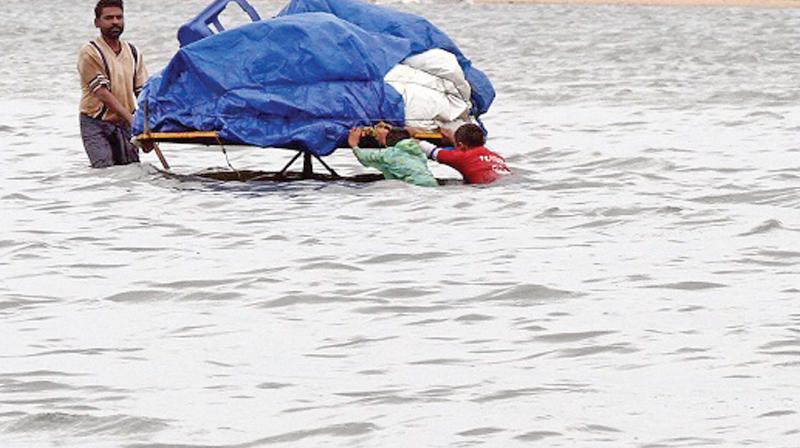 A vendor trying to get his cart to safety with the help of  two boys in the flooded Marina beach. (Photo: DC)