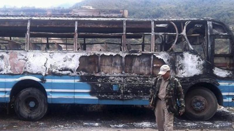 Police personnel walks infront of a charred bus burnt down by bandh supporters of United Naga Council, at Senapati, Manipur. (Photo: PTI)