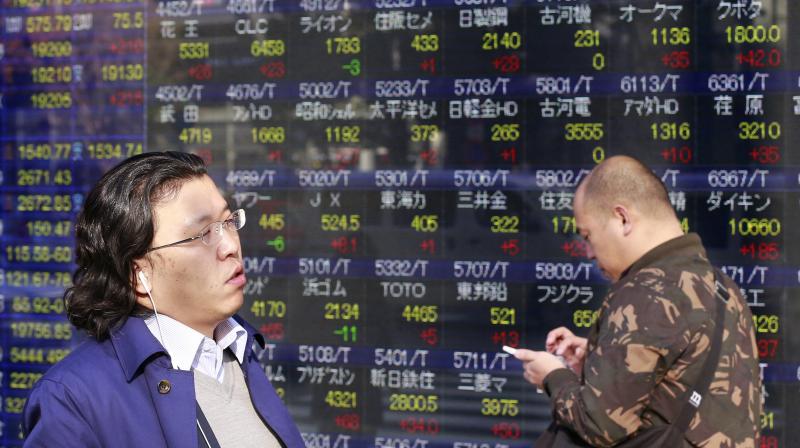 People walk past an electronic stock indicator of a securities firm in Tokyo. (Photo:AP)