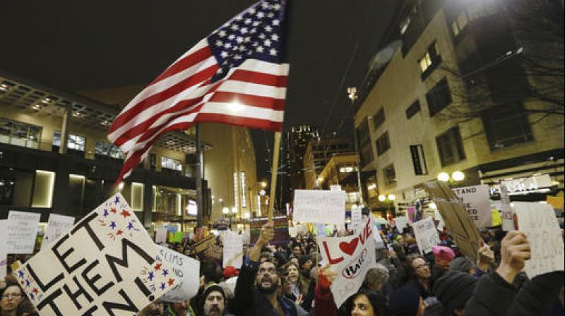 A protester waves a US flag as another holds a sign that reads \Let Them In\ during a march and rally to oppose President Donald Trumps executive order barring people from certain Muslim nations from entering the United States in Seattle. (Photo: AP)