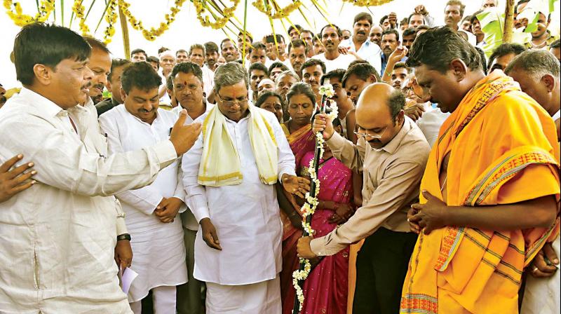 Chief Minister Siddaramaiahs son Dr Yathindra launches a project in Mysuru on Friday as the CM looks on.