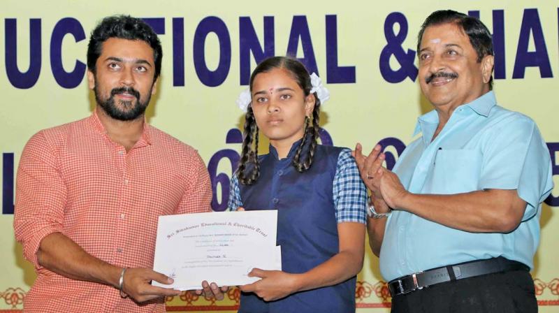 Actor Suriya awards a merit certificate to a student as dad and veteran actor Sivakumar applauds.
