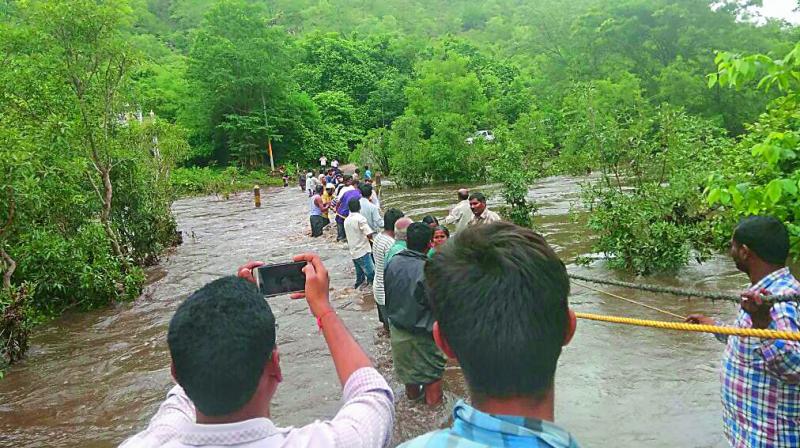 People cross a river with the help of a rope in Markapuram as heavy rains lash Prakasam district on Wednesday. (Photo: DC)