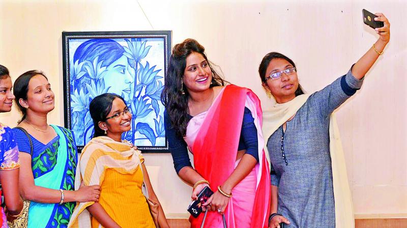 Art lovers and students take selfies with the paintings installed at Art @ Andhra in Guntur on Wednesday.