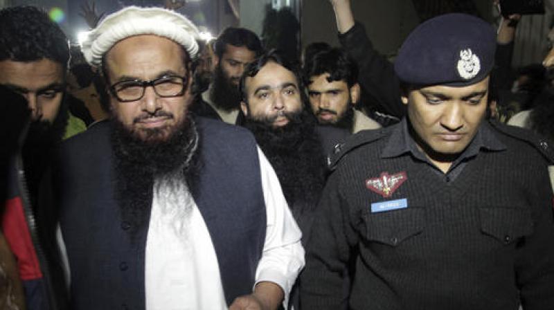 A Pakistani police officer escorts Hafiz Saeed, Chief of Pakistans religious group Jamaat-ud-Dawa outside partys headquarters in Lahore. (Photo: AP)