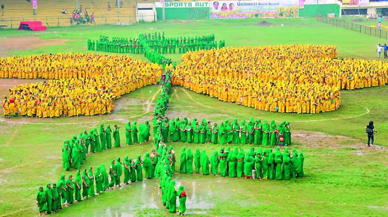 Women dressed in yellow and green saris stand in the shape of the Thangedu flower, which is the state flower, at the LB stadium on Thursday. 	(Photo: P. Anil Kumar )