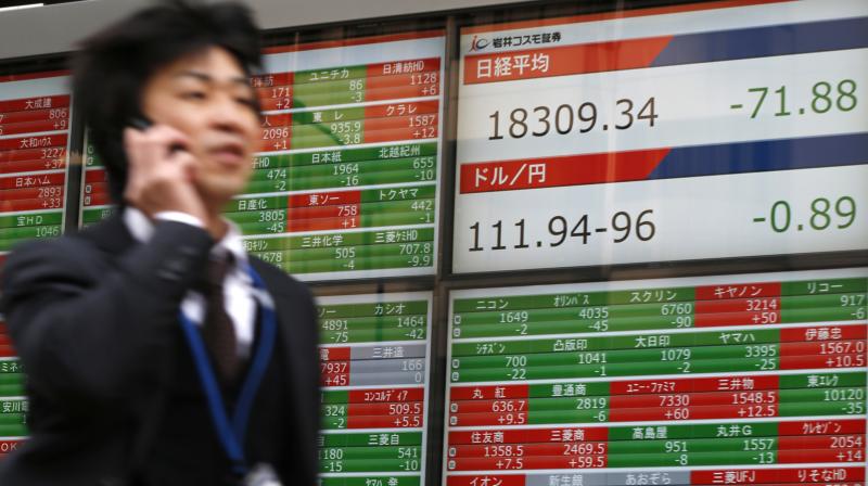 A man walks past the electronic board showing Nikkei stock index, right top, at a securities firm in Tokyo. (Photo:AP)