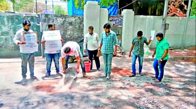 Residents of Marredpally fill holes on a street in the locality holding signs protesting GHMCs inaction.  (Image: DC)